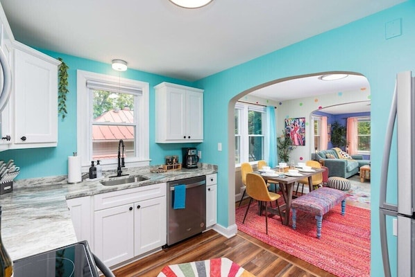 Una cocina moderna con armarios blancos, encimera de mármol y comedor con alfombra roja y sillas coloridas.