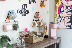 Una pared con tazas colgadas en un perchero, una cesta con aperitivos y una máquina de café sobre una mesa de madera.