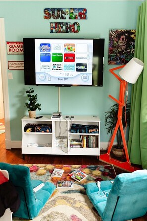 Un salon avec un téléviseur à écran plat fixé au mur, un meuble de rangement blanc en dessous et un tapis coloré sur le sol.
