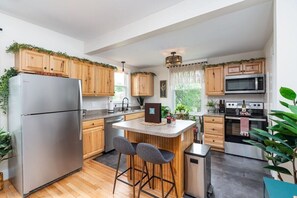 Eine moderne Küche mit Holzausstattung, einem Edelstahlkühlschrank, einer Mikrowelle und einer integrierten Kücheninsel mit Barhocker.