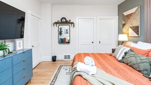 Quarto com cama, penteadeira, televisão e espelho fixado na parede.