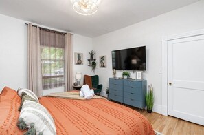 A bedroom with a large bed, a TV, a dresser, and a window with curtains.