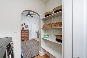 Ein Flur mit Deckenventilator, einem gemusterten Teppich und Regalen mit gewebten Körben.