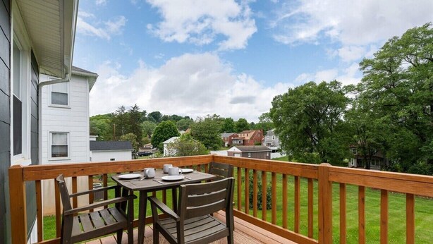Um deck de madeira com mesa e cadeiras, com vista para uma área residencial com casas e árvores.