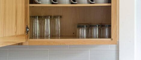 Un mueble de cocina con estantes que contienen tazas de cerámica blanca y frascos de vidrio.