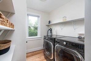 A laundry area with two front-loading washing machines, a window, and shelves with baskets and a jar.