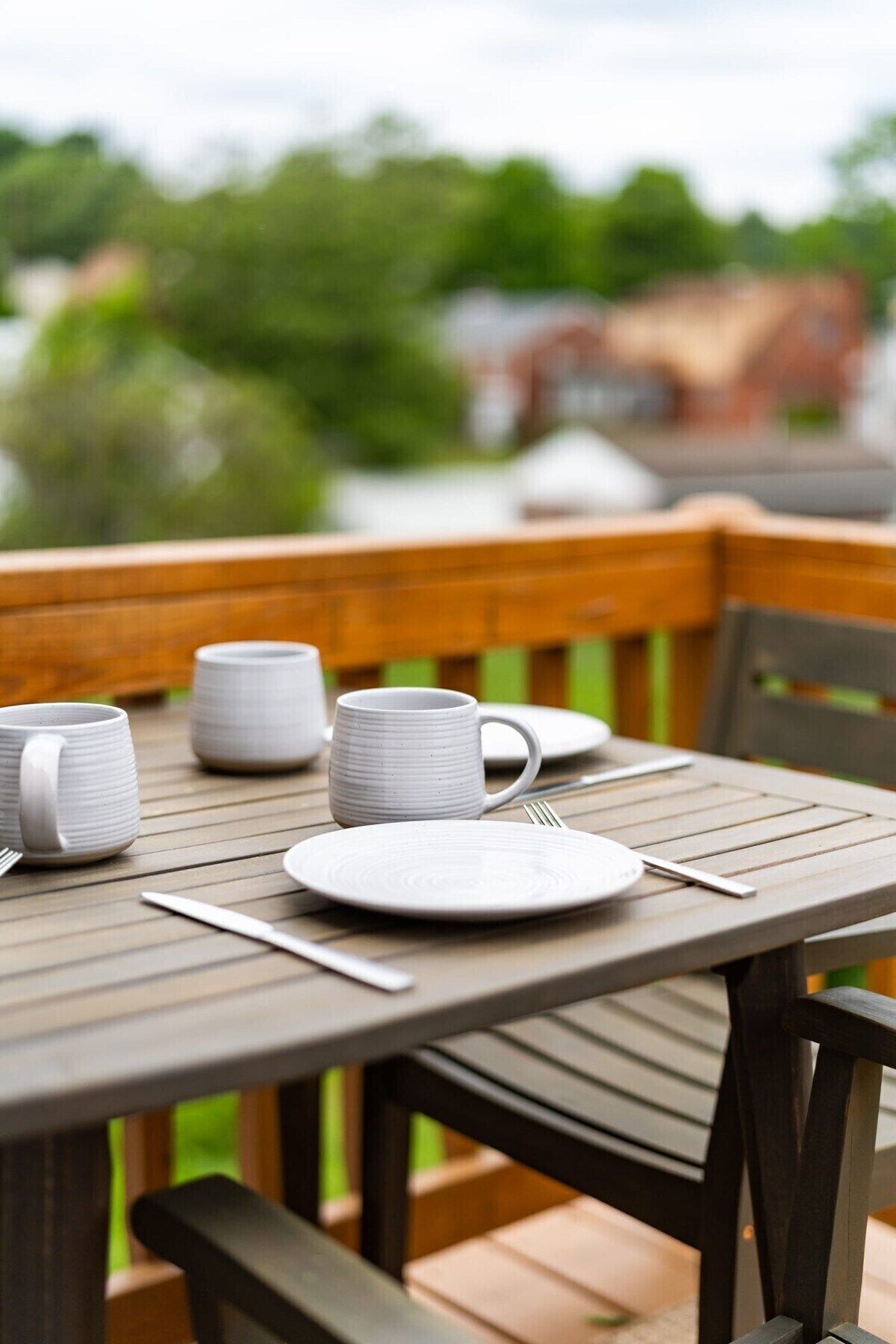 A wooden deck with a table set for dining, including plates, cups, and cutlery.