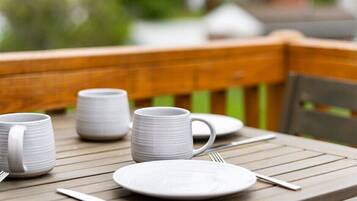 A wooden deck with a table set for dining, including plates, cups, and cutlery.