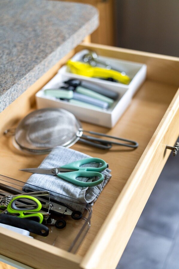 Un cajón con varios utensilios de cocina, incluyendo un colador, unas tijeras y un recipiente amarillo.