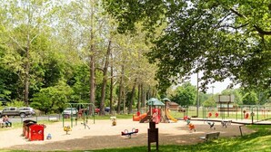 Um parque com equipamentos de playground, mesas para piquenique e uma área cercada.