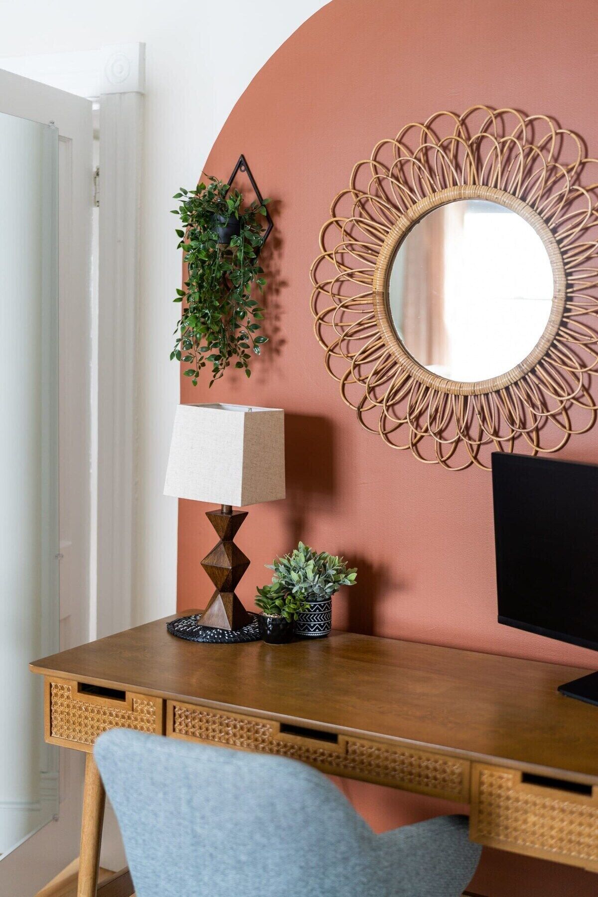A wooden desk with a lamp, a potted plant, and a mirror on the wall.