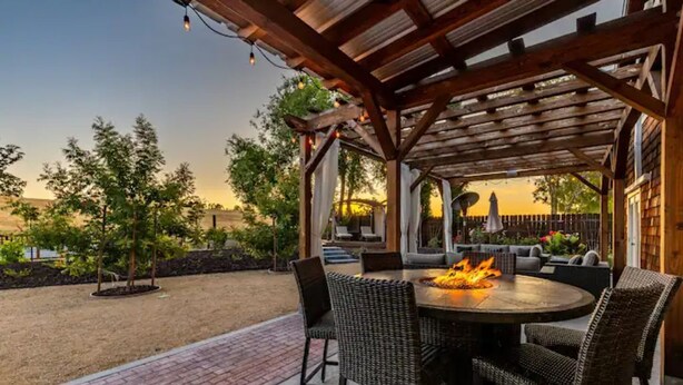 Une terrasse extérieure avec une table ronde et des chaises, un foyer et une structure en forme de pergola.