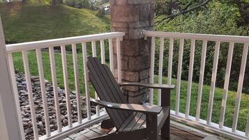 A wooden deck with a stone pillar, a white railing, and a single Adirondack chair.