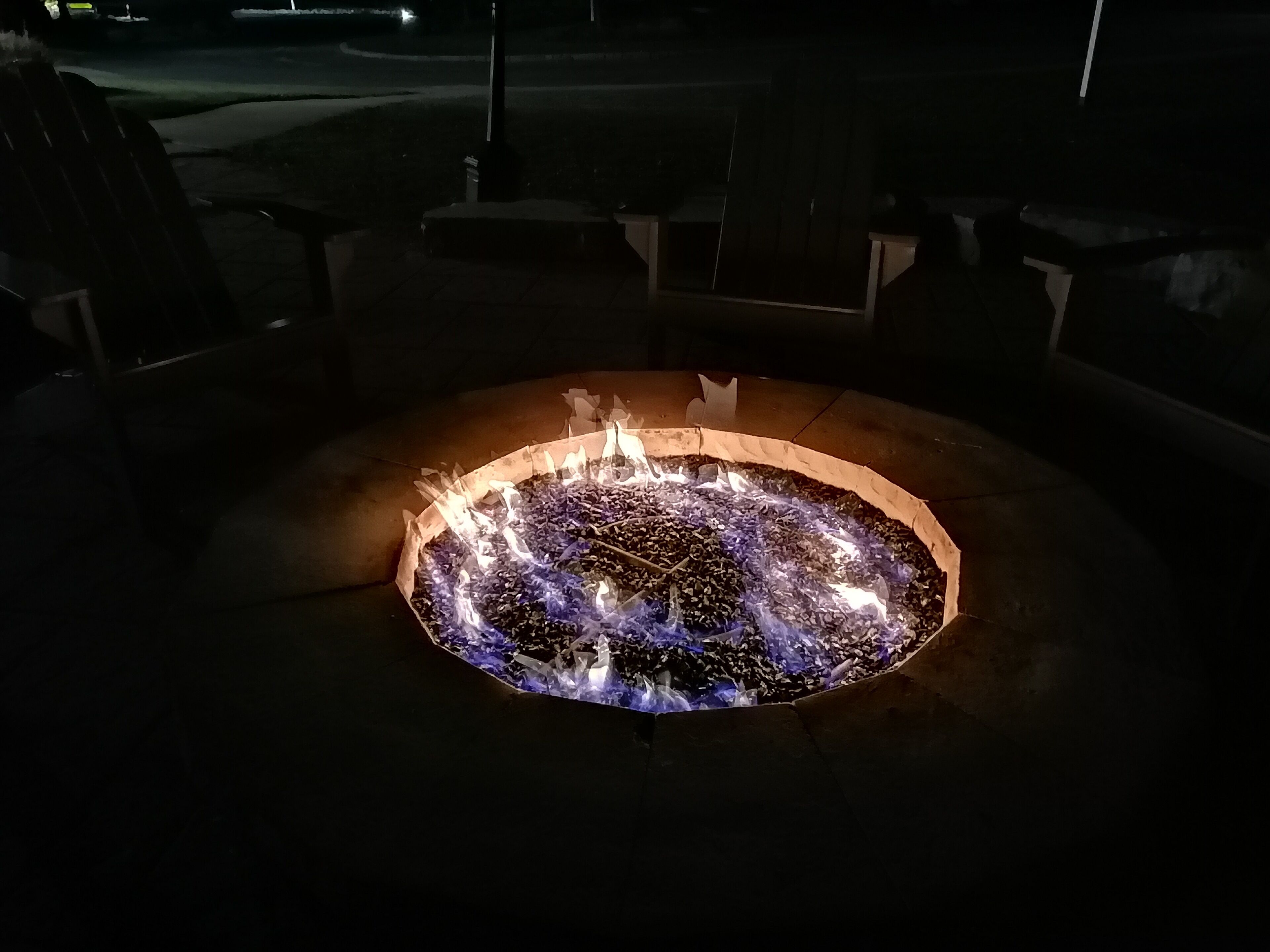 A circular outdoor fire pit with flames, surrounded by stone seating.