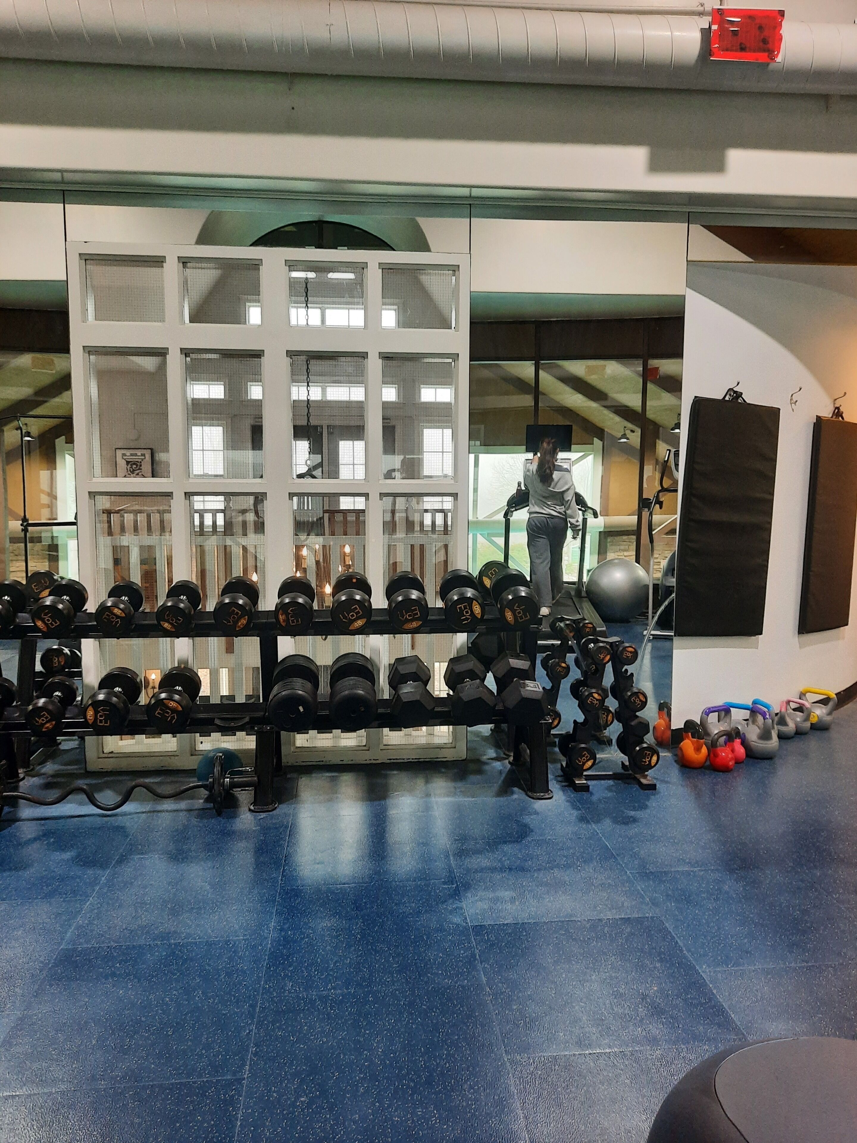 A gym with various weightlifting equipment, including dumbbells and kettlebells, and a person exercising.