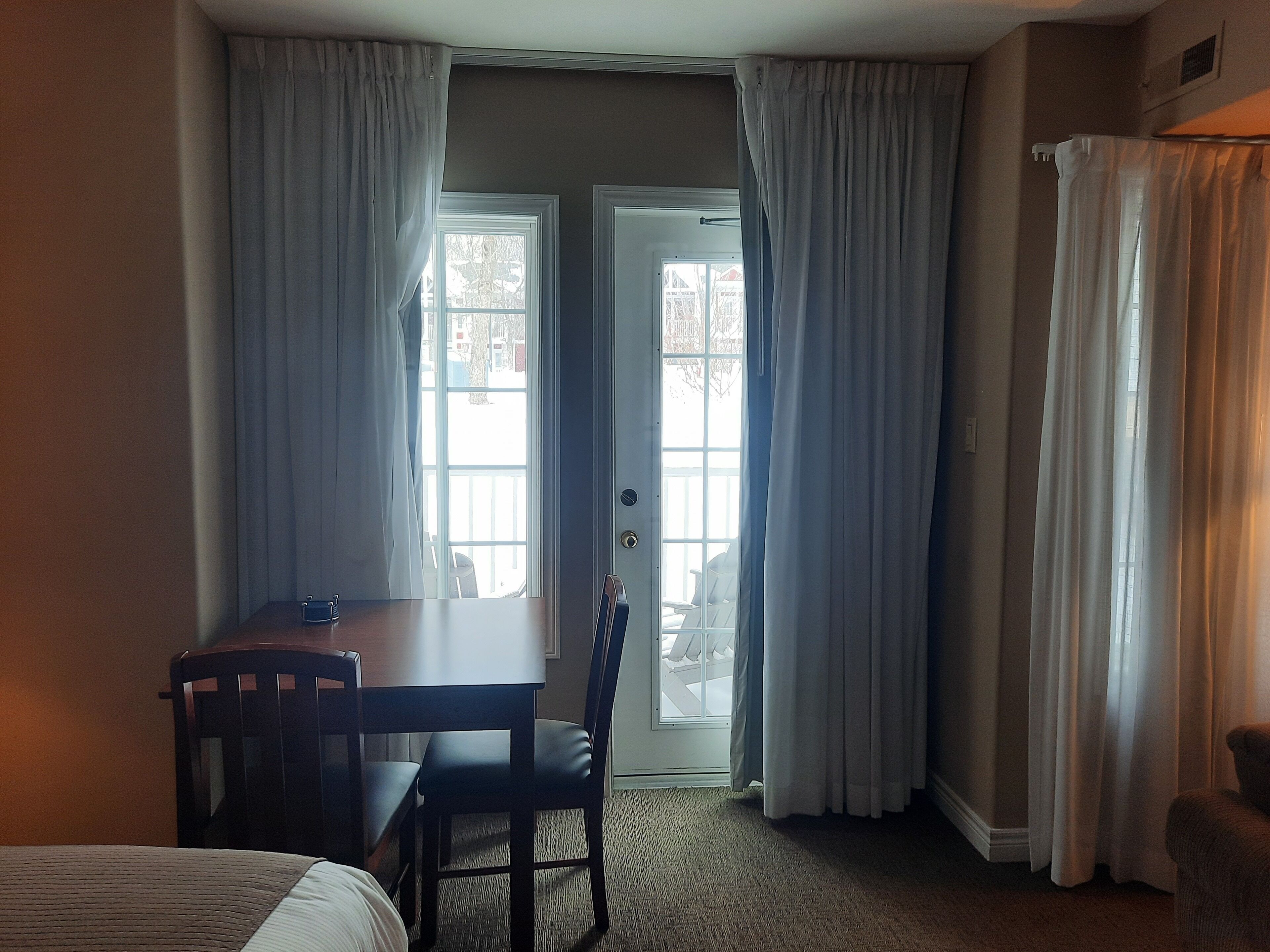 A room with a wooden table and a chair, a door leading outside, and a view of the outside through the door.