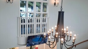 A grand staircase with a chandelier, a large window with a white frame, and a flat-screen TV mounted on the wall.