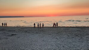A beach with people standing on the sand, facing the ocean during sunset.
