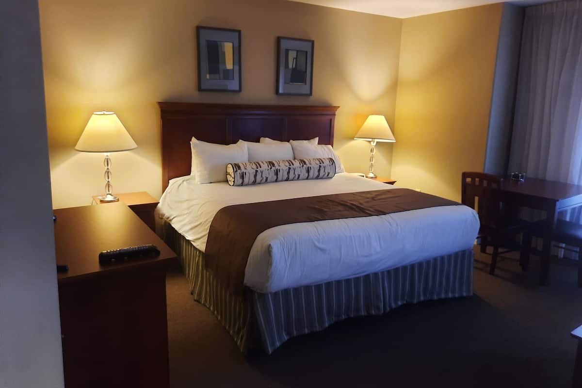 Ein Hotelzimmer mit einem großen Bett, zwei Nachttischlampen, einem Holzkopfteil, einem Schreibtisch mit Stuhl und zwei gerahmten Bildern an der Wand.