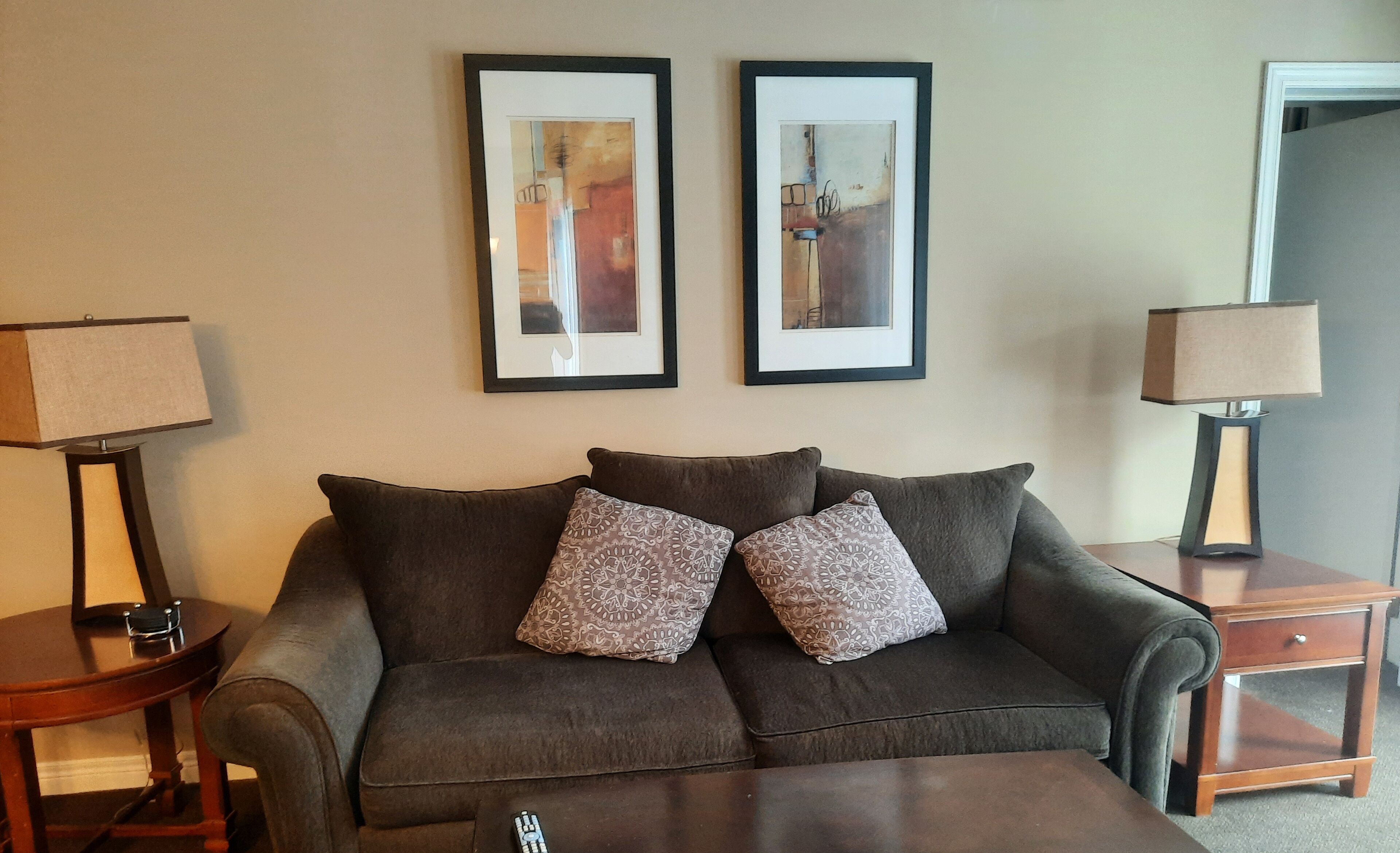 A living room with a grey sofa, two patterned throw pillows, a small wooden side table, and a lamp.