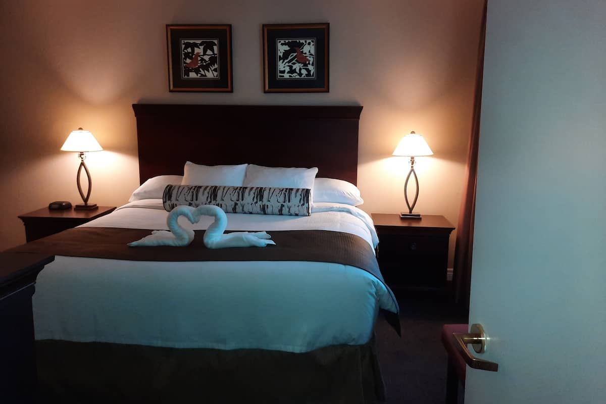 Ein Hotelzimmer mit einem Bett, zwei Nachttischen, zwei Wandlampen und zwei Bildern im Bilderrahmen über dem Bett.