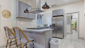 A modern kitchen with grey cabinets, a stainless steel refrigerator, and two wicker chairs with blue cushions. - Welcome to Casa Azul 1932 Eclectic Boho Sanctuary  in Downtown Riverside! (Riverside)