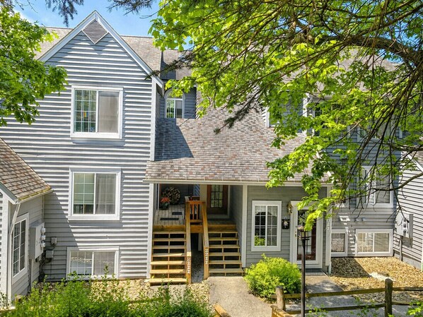 A two-story house with a front porch, a wooden staircase, and a small garden area.