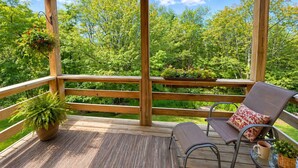 Een houten terras met een balustrade, twee stoelen en plantenbakken.