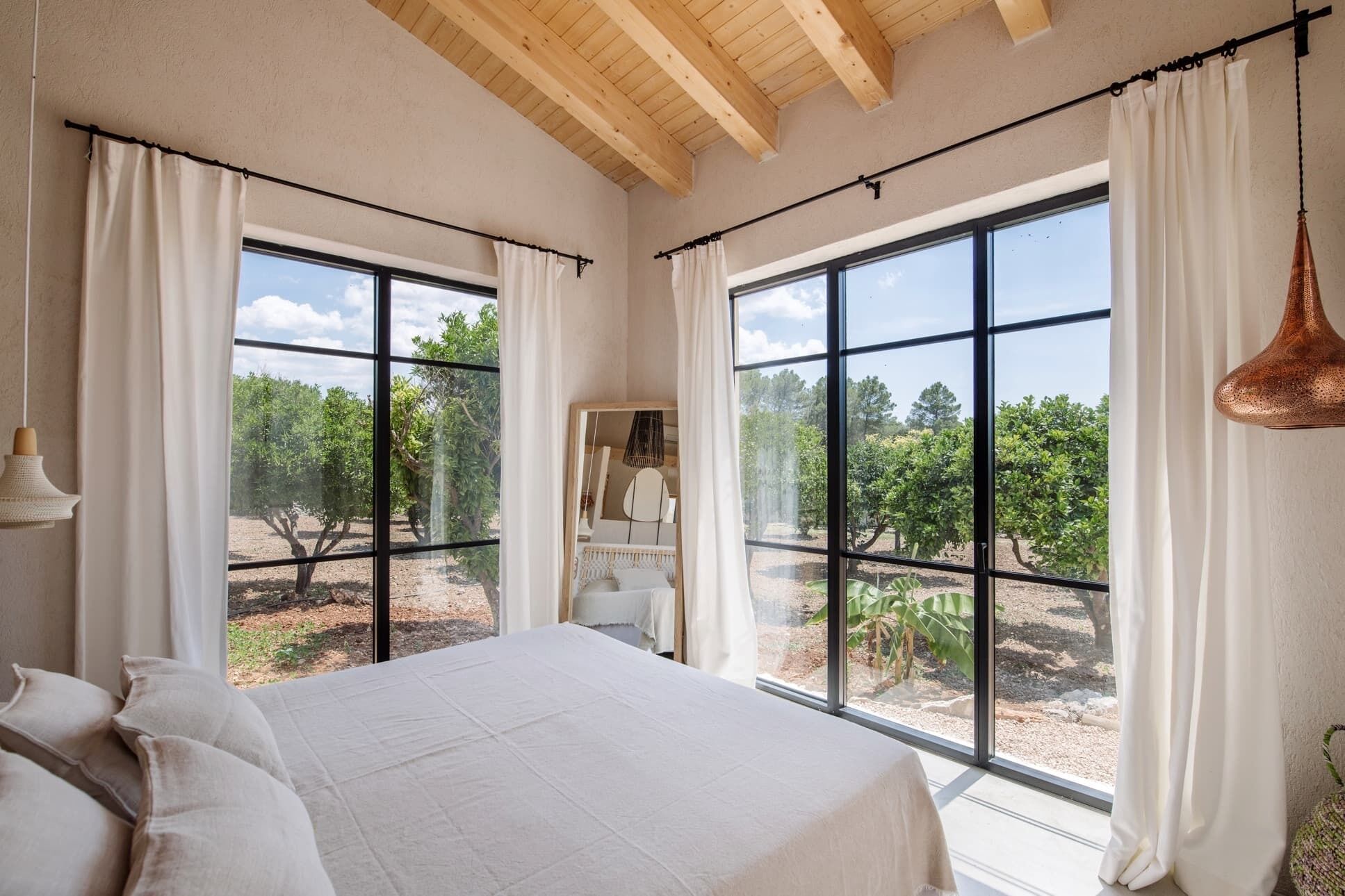 Quarto com cama grande, duas janelas e vista para um pomar.