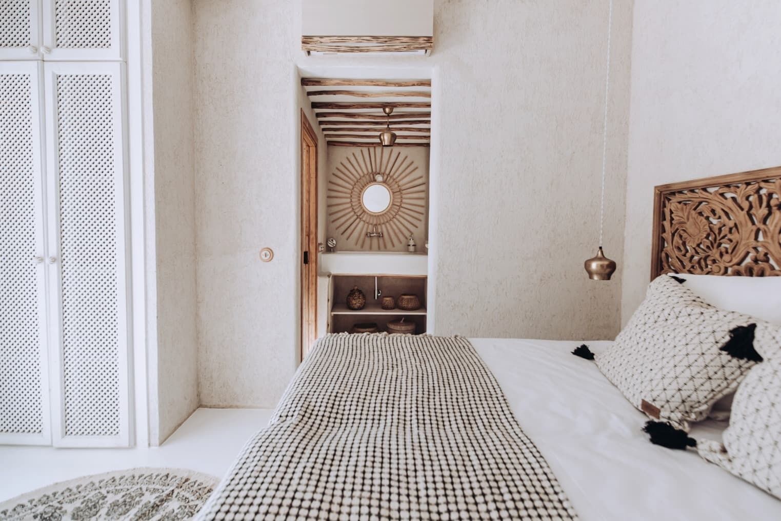 A bedroom with a bed, a wooden headboard, a wall-mounted mirror, and a shelf with decorative items.