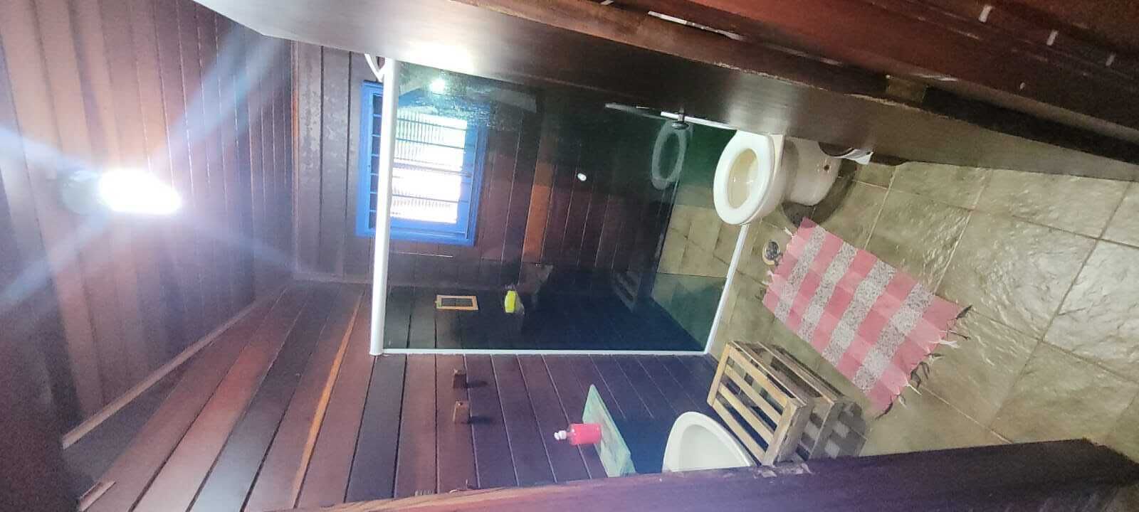Um banheiro pequeno e rústico com piso de madeira, uma janela com barras azuis, vaso sanitário e pia.
