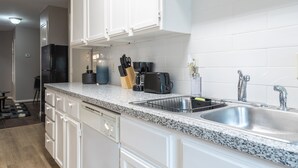 Una cocina moderna con armarios blancos, encimeras de granito, un lavamanos de acero inoxidable y una cafetera.