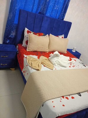 Un letto con copripiumino rosso e bianco a motivi floreali, due cuscini color beige e una testiera blu.