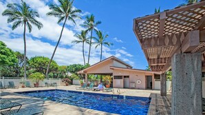 A swimming pool with lounge chairs, palm trees, and a covered area with a pergola. - Budget Friendly - Kihei Akahi C-608, Ocean Views, Short Walk to Kamaole Beach II (Kihei)