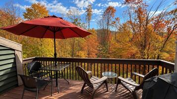 A wooden deck with outdoor furniture, including chairs and a table, and a red umbrella.