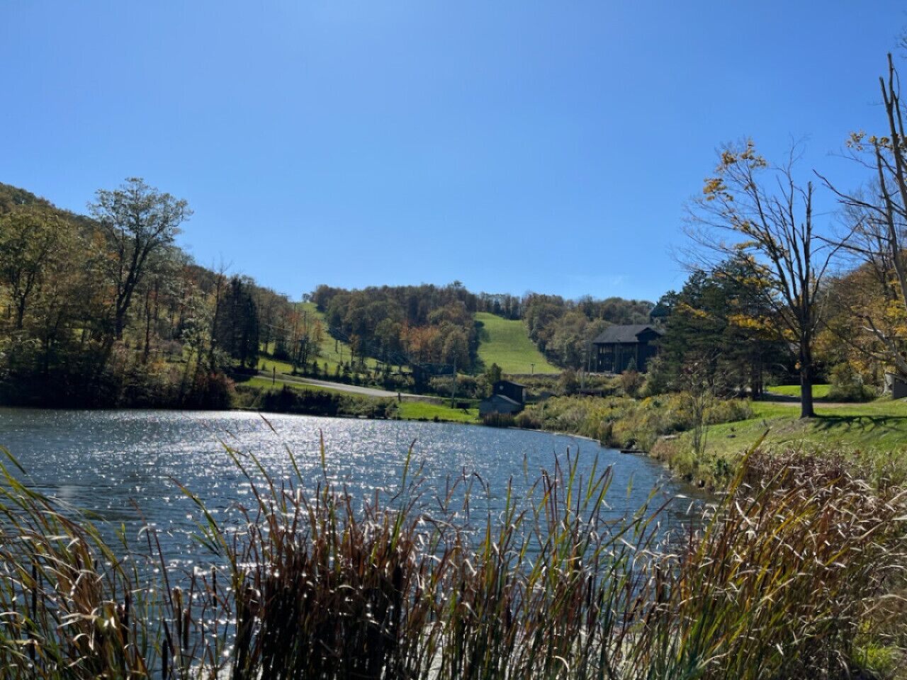 A serene lakeside view with a house on the right and a forested hill on the left.