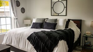 A bedroom with a large bed, a bedside table with a lamp, and a window with curtains. - The Leland Blue on M-22 (Suttons Bay)