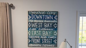 A room with a wall-mounted sign listing various locations, a potted plant, a lamp, and a chair. - The Leland Blue on M-22 (Suttons Bay)