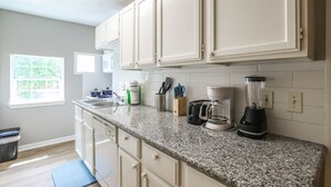 Una cocina con alacenas blancas, encimera de granito, licuadora y cafetera.