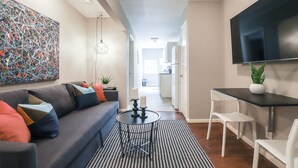 Un salón moderno con un sofá gris, una mesa de centro negra y un televisor de pantalla plana montado en la pared.