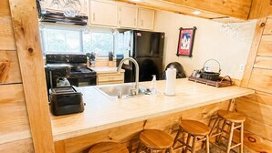 A wooden cabin interior with a kitchen, bar stools, and a dining table.