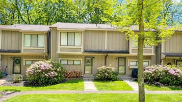Une rangée de maisons de ville à deux étages, dotées d’une entrée centrale, d’un jardin devant et d’un arbre au premier plan.