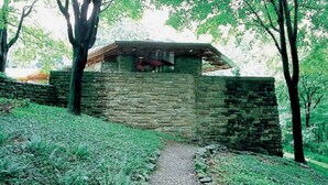 A stone building with a sloped roof, surrounded by trees and a grassy path.