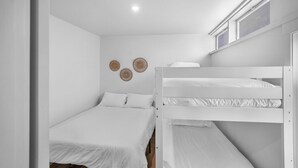 A bunk bed room with white bedding, a small window, and wall decor. - Riverside Suite | Kitchenette, Firepit & BBQ (Lake Cowichan)