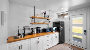A modern kitchen with white cabinets, a wooden countertop, a black refrigerator, a coffee maker, and a microwave. - Riverside Suite | Kitchenette, Firepit & BBQ (Lake Cowichan)