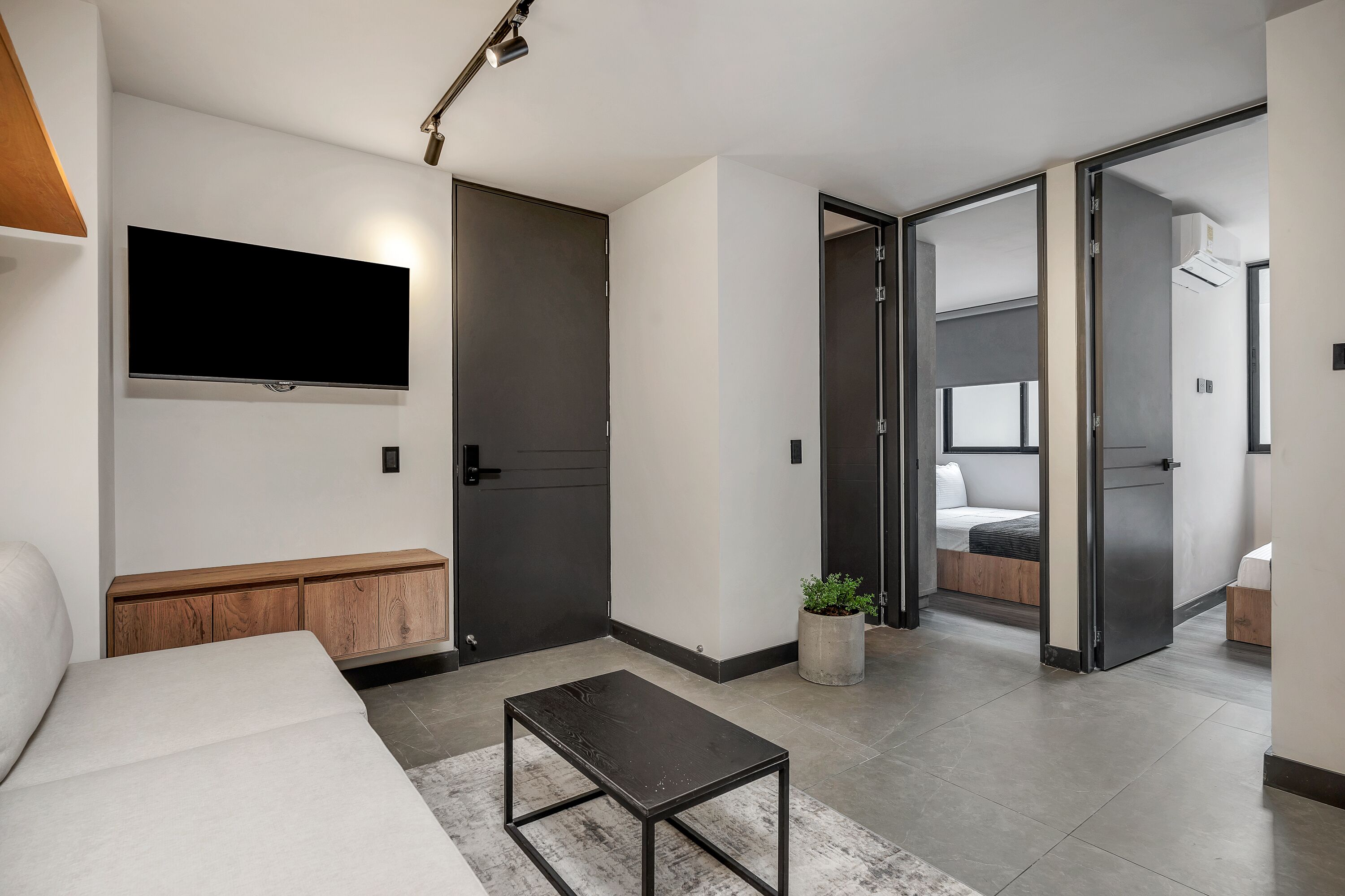 Ett modernt hotellrum med en platt-TV, en träbänk, ett litet bord och en säng med en sänggavel.