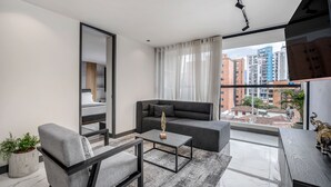 Un salon moderne comprenant un canapé, un fauteuil, une table basse et une grande fenêtre donnant sur la ville.