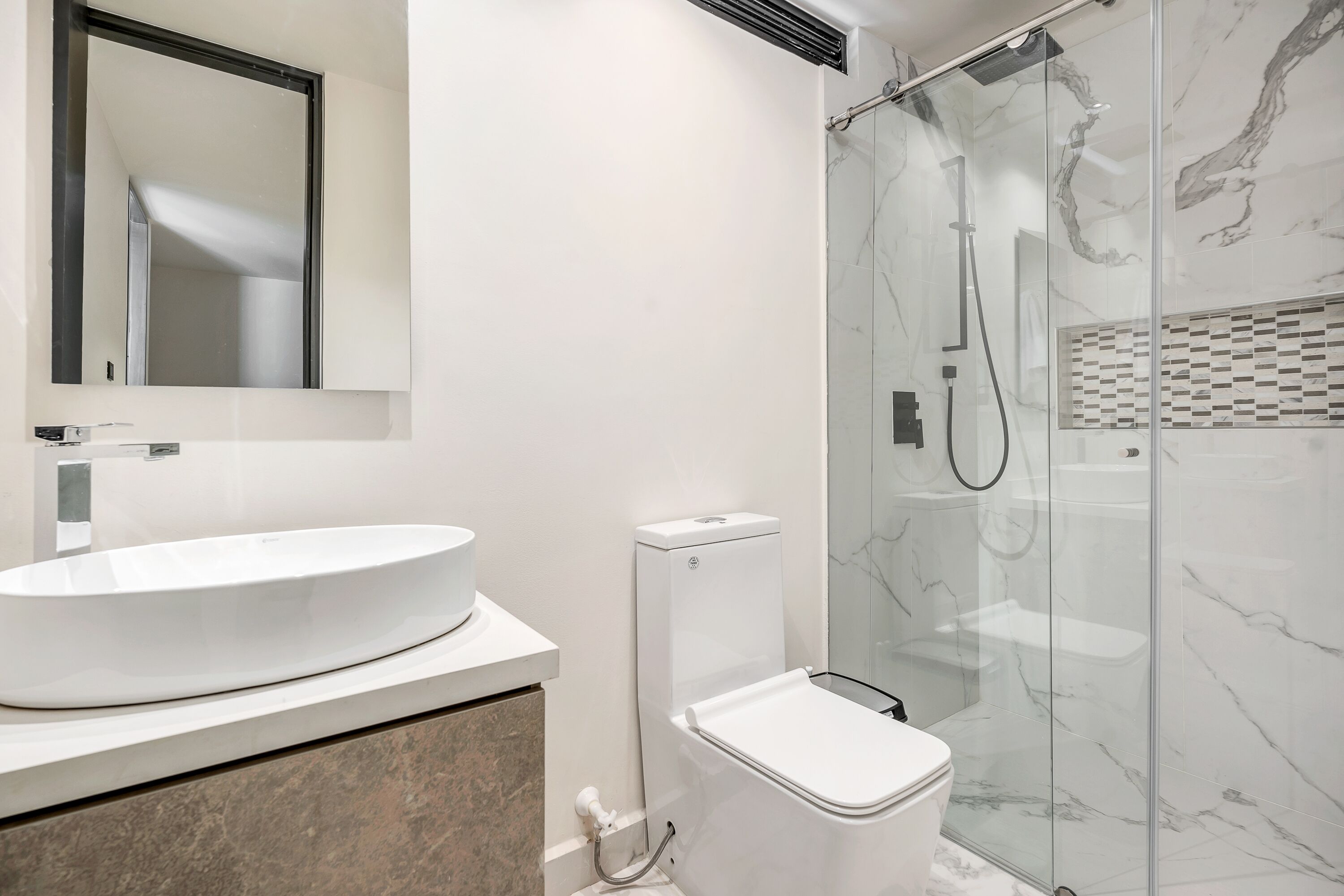 A modern bathroom with a large white sink, a toilet, and a glass-enclosed shower area.