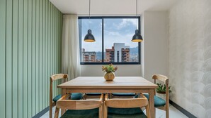 Un coin repas avec une table et des chaises en bois, un vase rempli de fleurs et une vue sur les bâtiments, visible à travers une grande fenêtre.