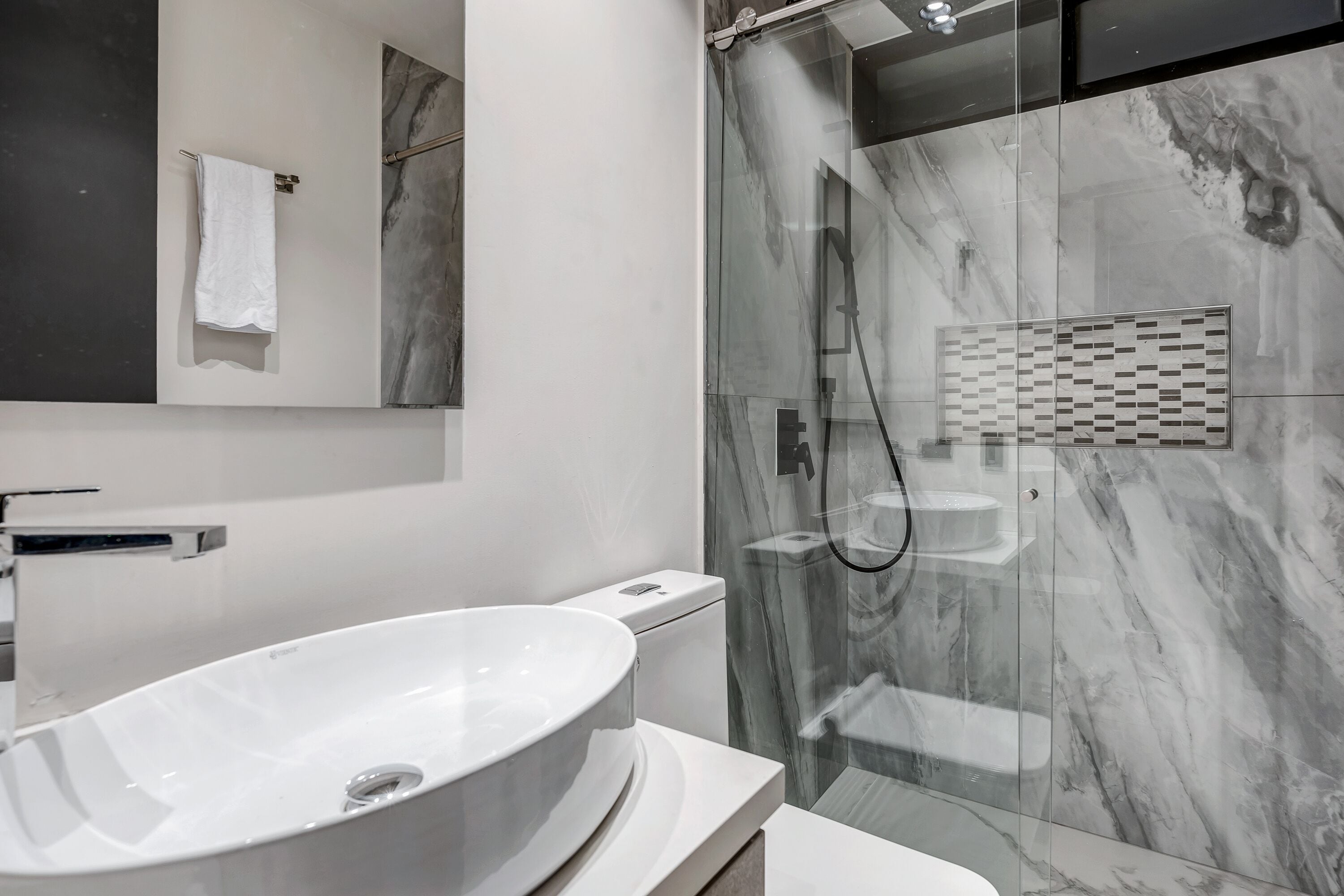 A modern bathroom with a white sink, a glass-enclosed shower, and a marble backsplash.